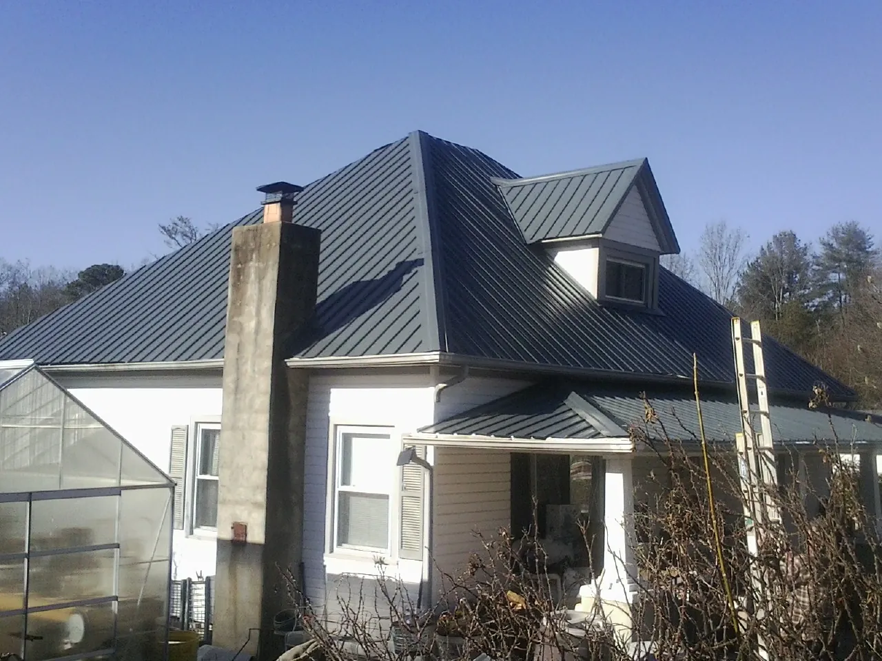Dark blue standing seam metal roof on a white farmhouse with dormer — Slate & Tile Roof Repair by Roofing Brothers in New Albin