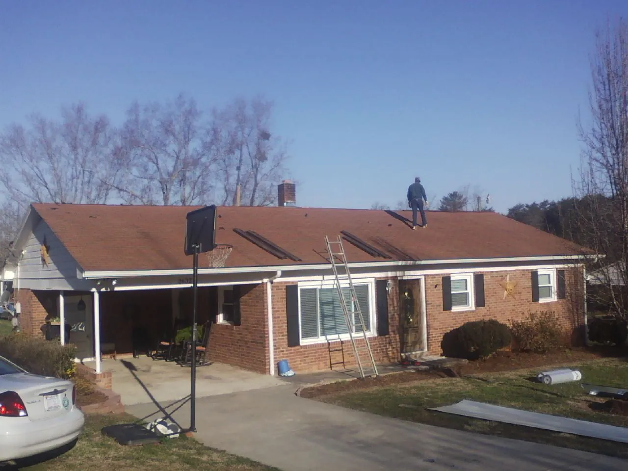 Roofer stripping a shingle roof on a brick ranch before metal panels in New Albin