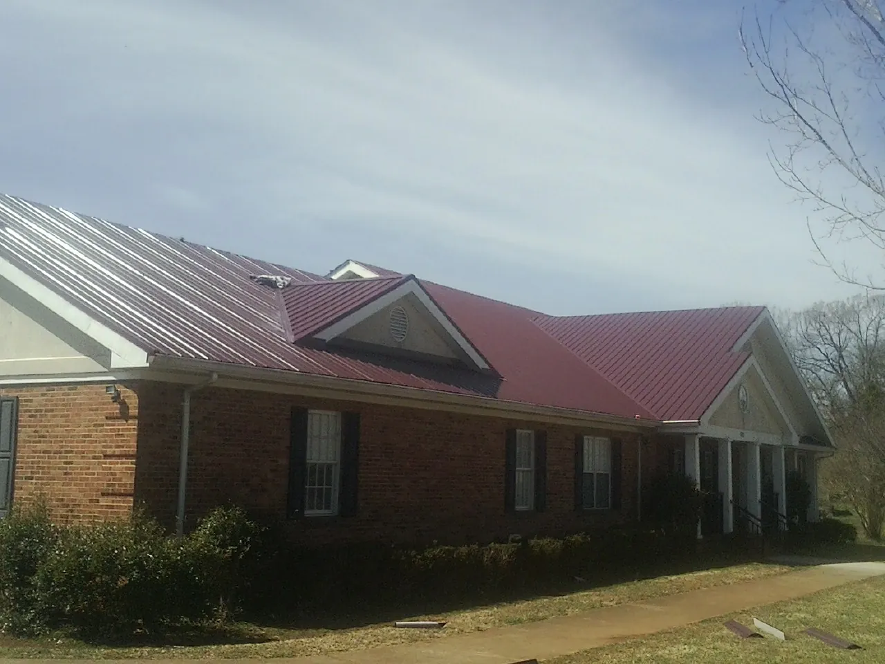 Red metal roof with gabled entries on a long brick building, from a Hail Damage Roof Repair job in New Albin