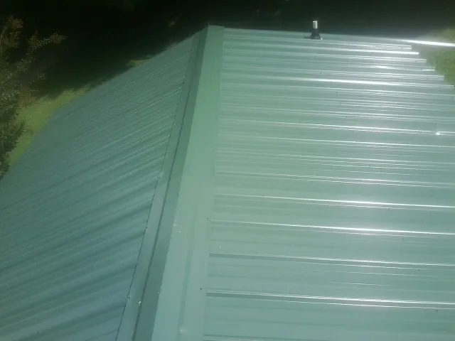 New green metal panels meeting at the ridge of a roof — Flat Roof Repair work by our crew in New Albin