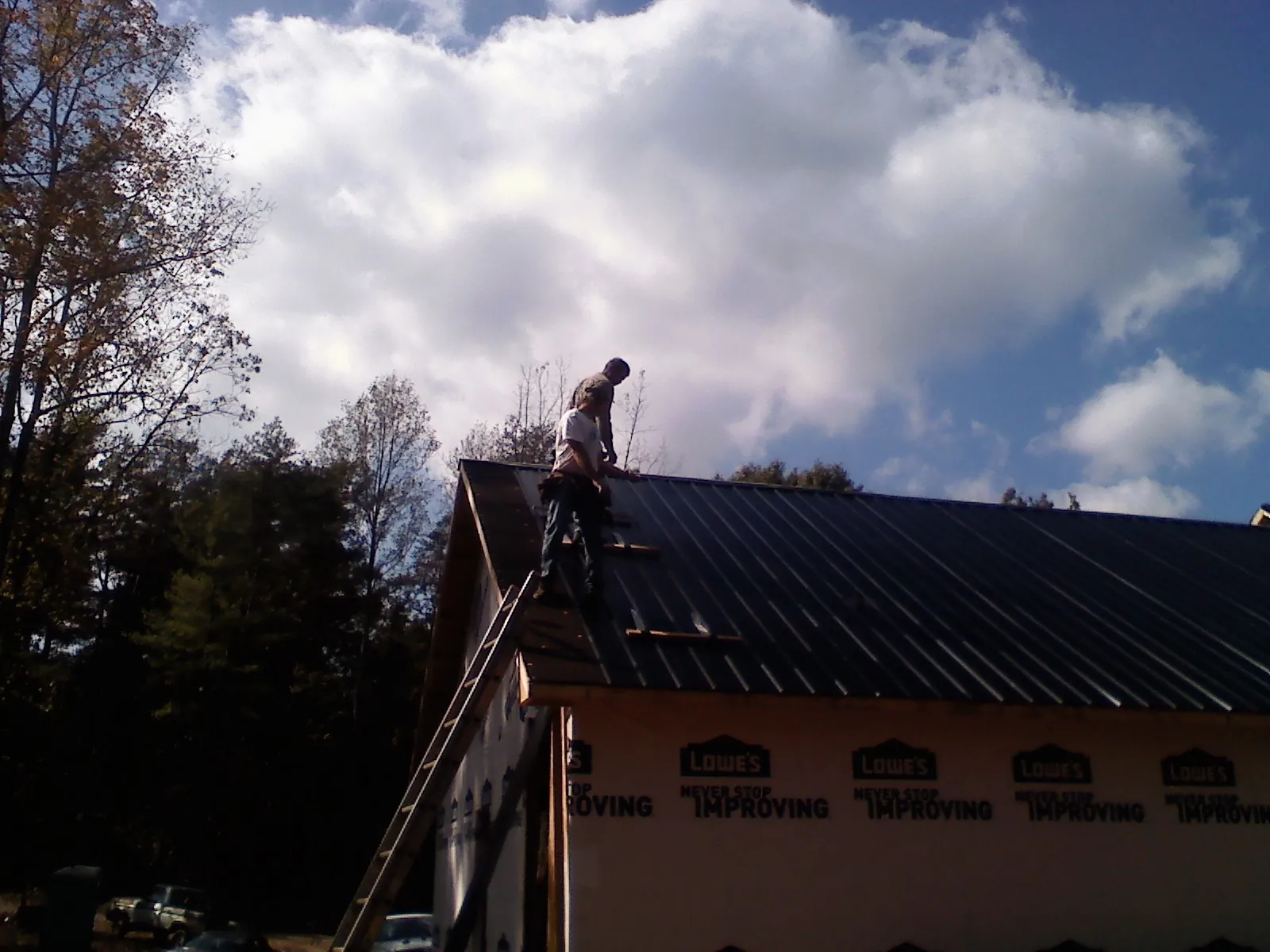 Roofer fastening dark metal panels high against a cloudy sky, from a Roof Inspection job in New Albin