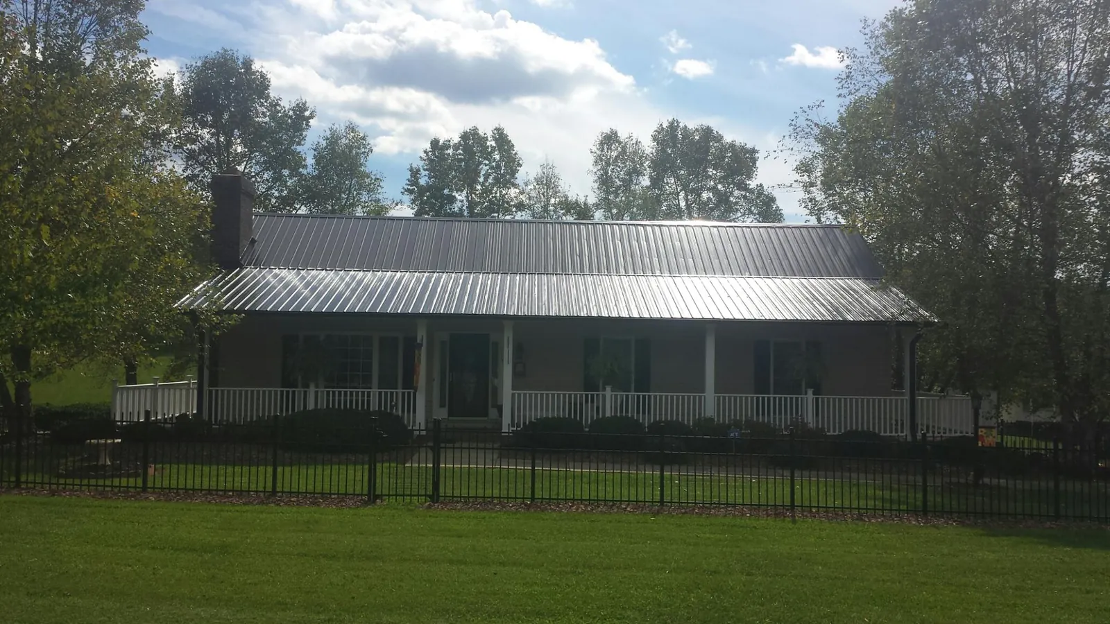 Gray metal roof on a brick ranch with a full width front porch — Gutter Guard Installation work by our crew in New Albin