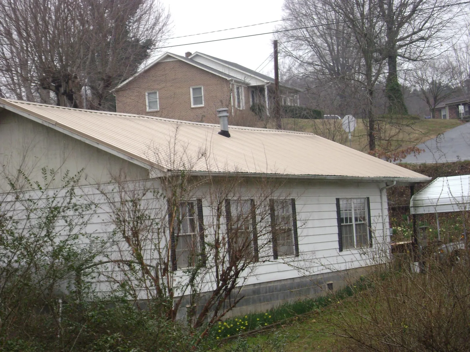 Tan metal roof on a white sided house set into a hillside — Commercial Roofing by Roofing Brothers in New Albin