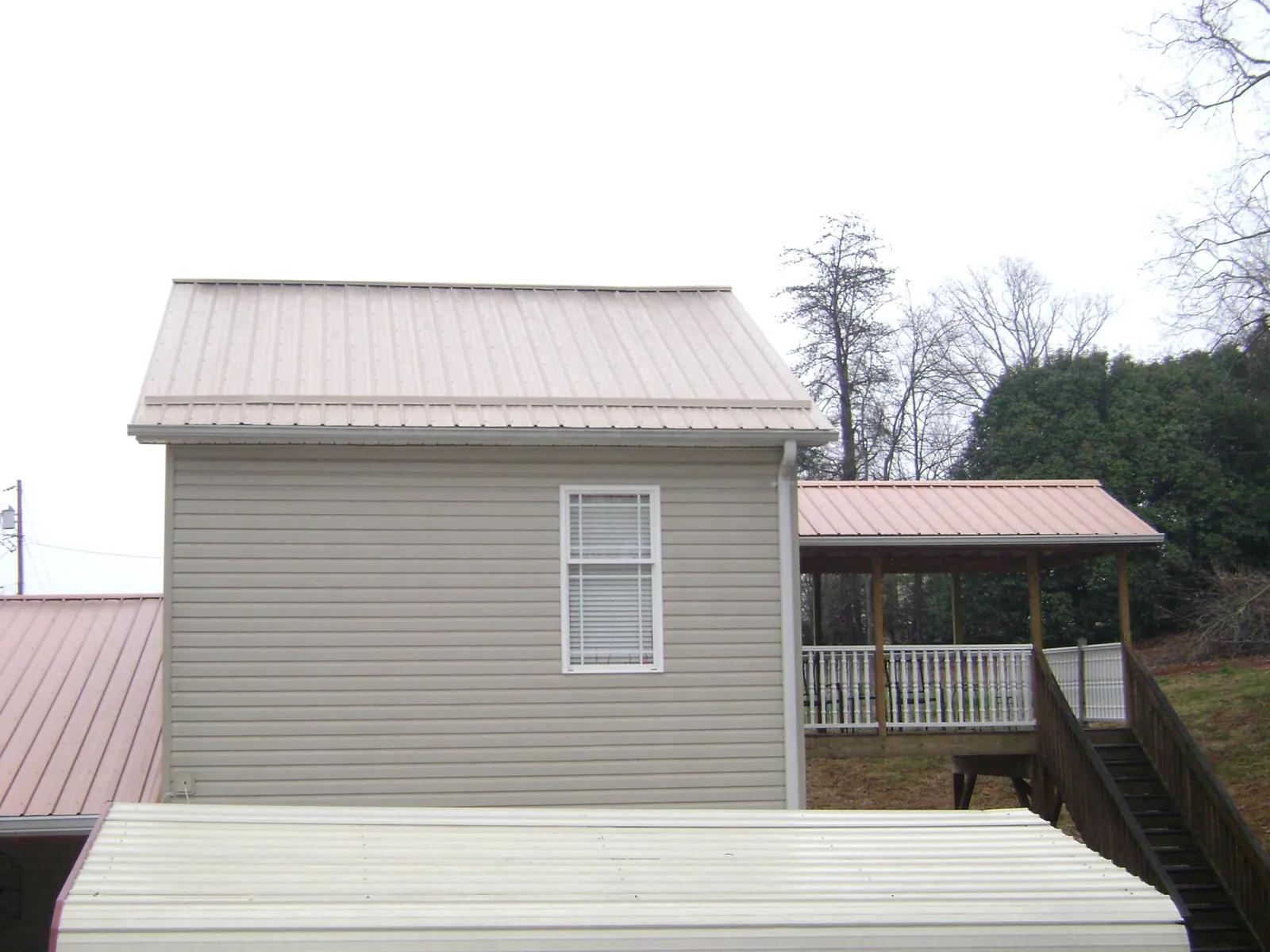 Tan metal roofs on a two story addition and attached porch, from a Roof Replacement job in New Albin